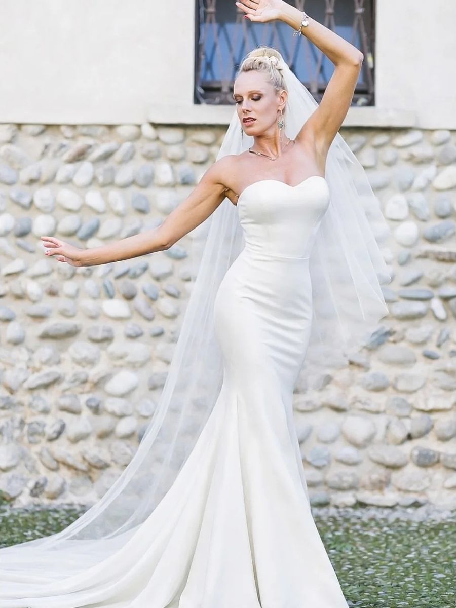 Abito da sposa a sirena con velo, davanti a un muro di ciottoli